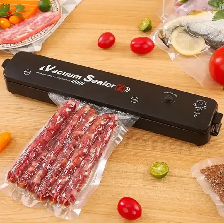 Вакуумний пакувальник Vacuum Sealer чорного кольору, компактний, на білому фоні, з вакуумним пакетом, що показує процес пакування.